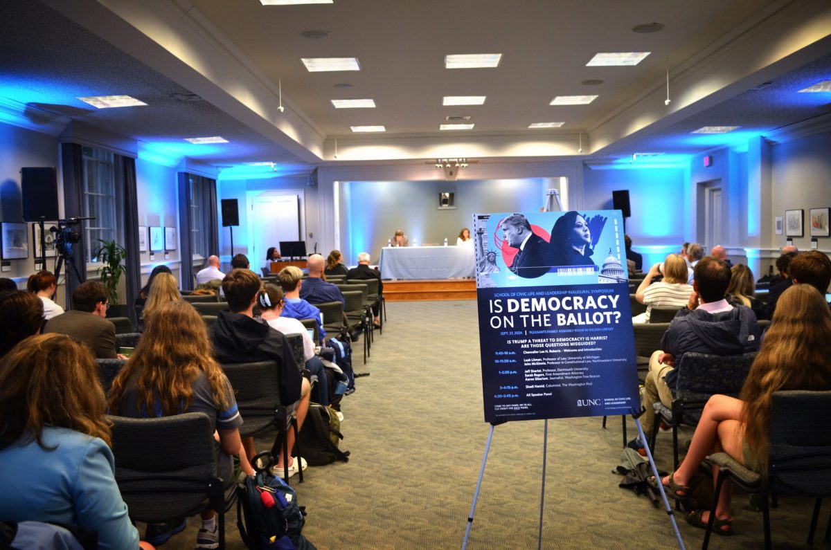 People sit in chairs at UNC-CH, a sign reads 'Is Democracy on the Ballot'