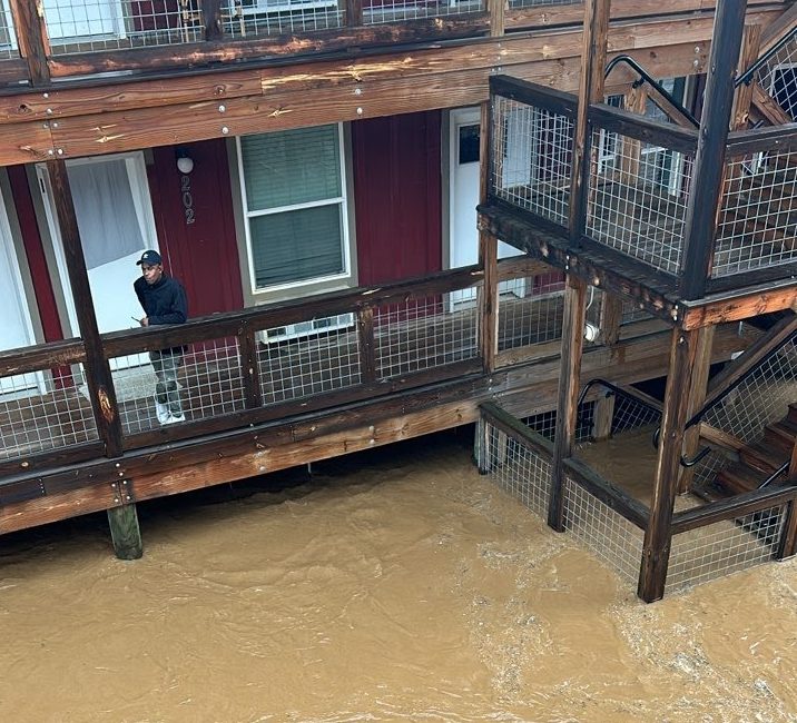 man looks off apartment walkway into brown floodwaters