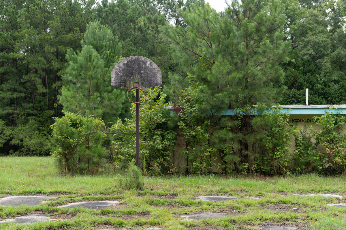 basketball rack with hoop falling off and an overgrown court