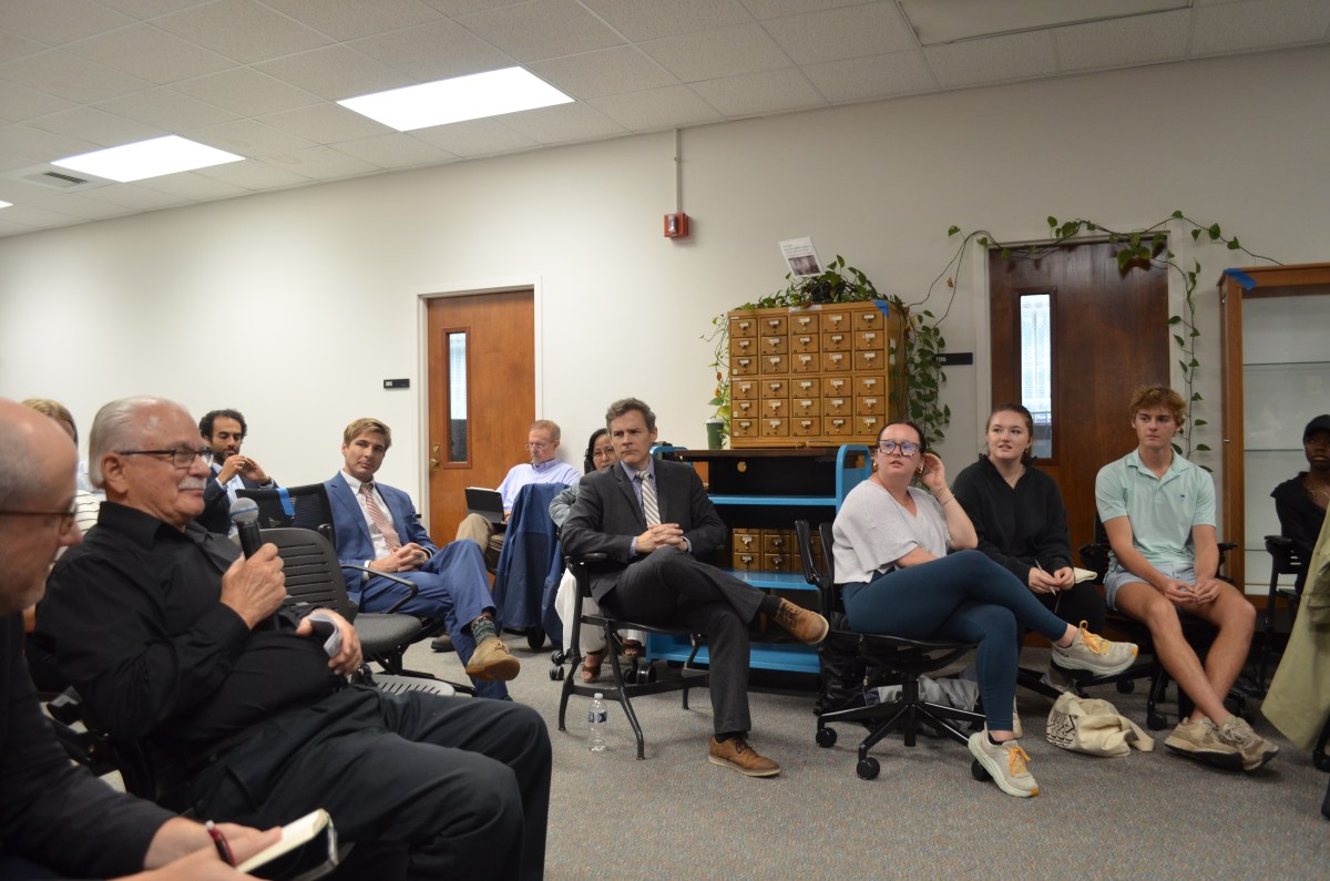 A group of people sit in chairs looking at a man holding a microphone
